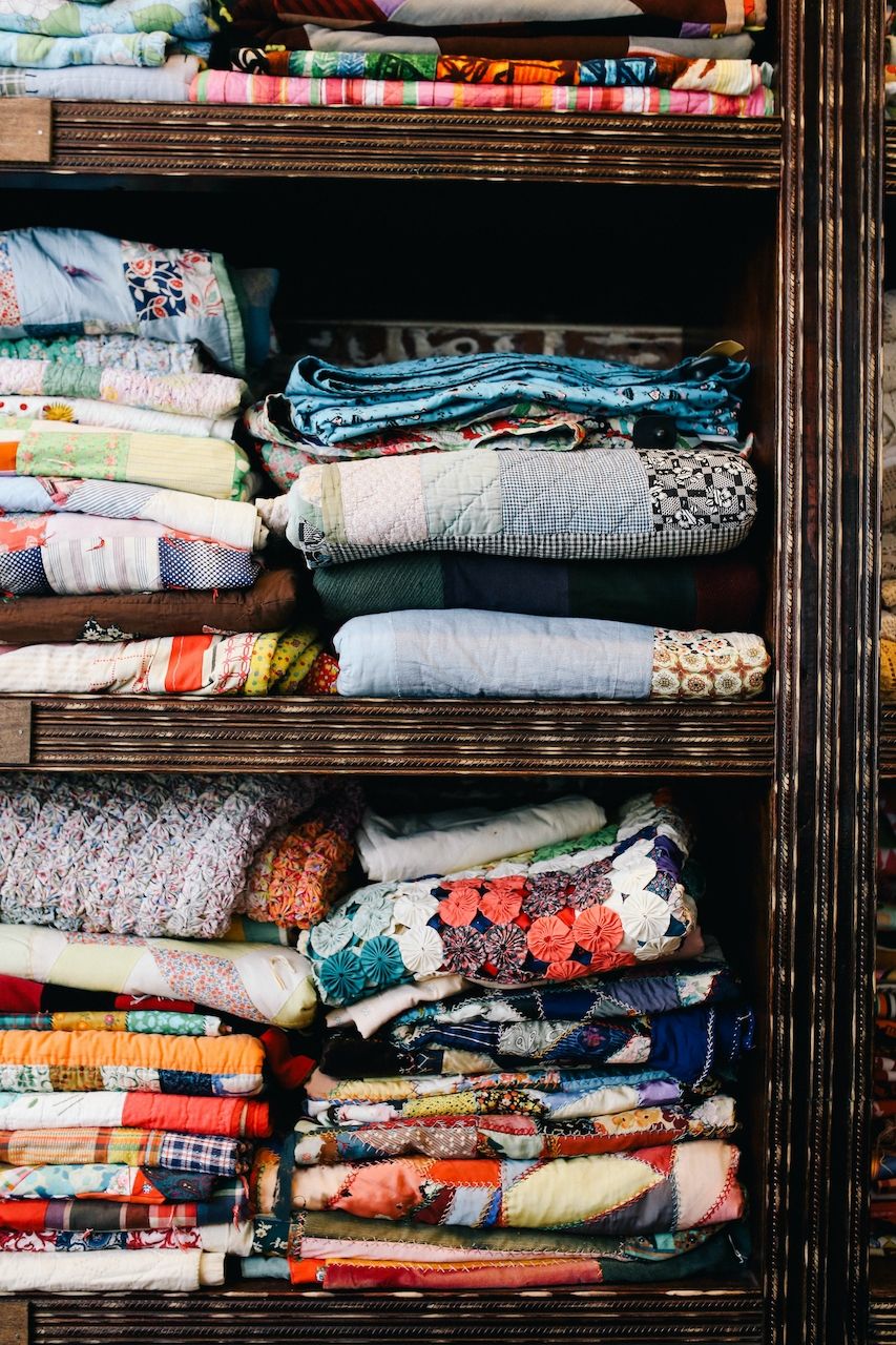 Two shelves up close packed full of colourful quilted fabrics. 